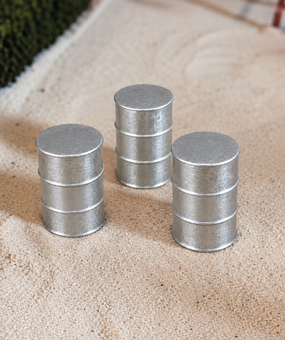 Three miniature silver metal barrel-shaped accessories standing upright on a beige sandy surface.