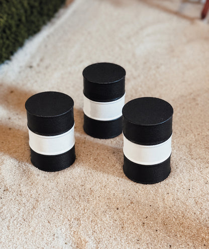 Three black and white striped cylindrical containers or candle holders arranged on a light beige textured surface.