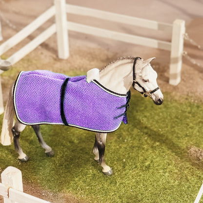 Horse wearing a purple rug in an outdoor setting with a white fence.