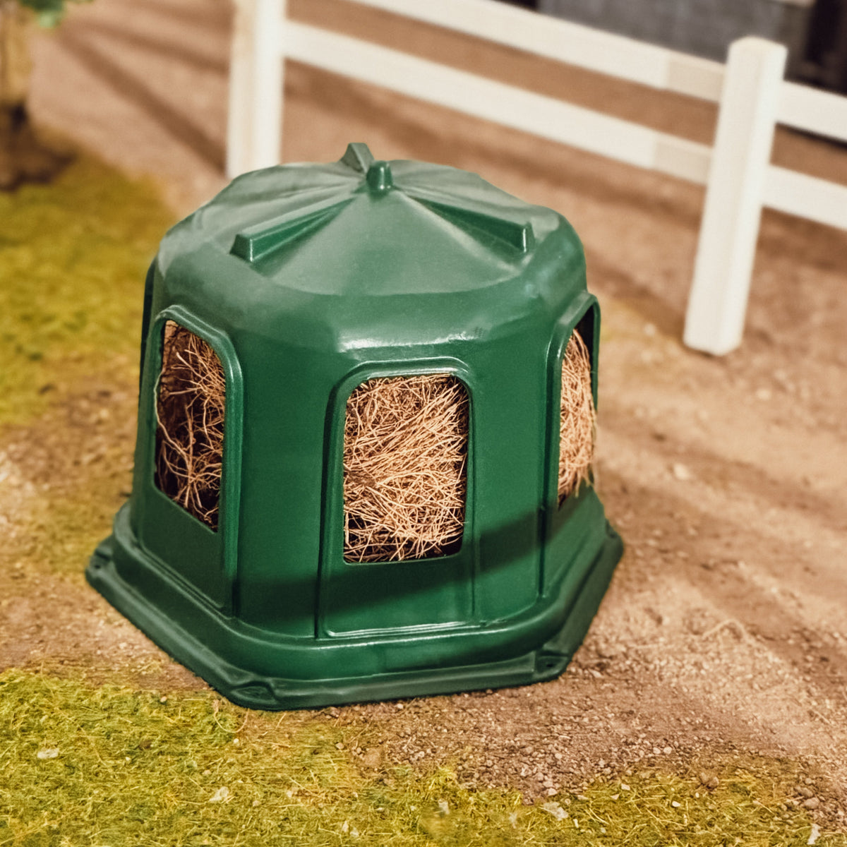 Green 3D printed hay bell feeder for Schleich model horses, filled with hay, standing in a paddock