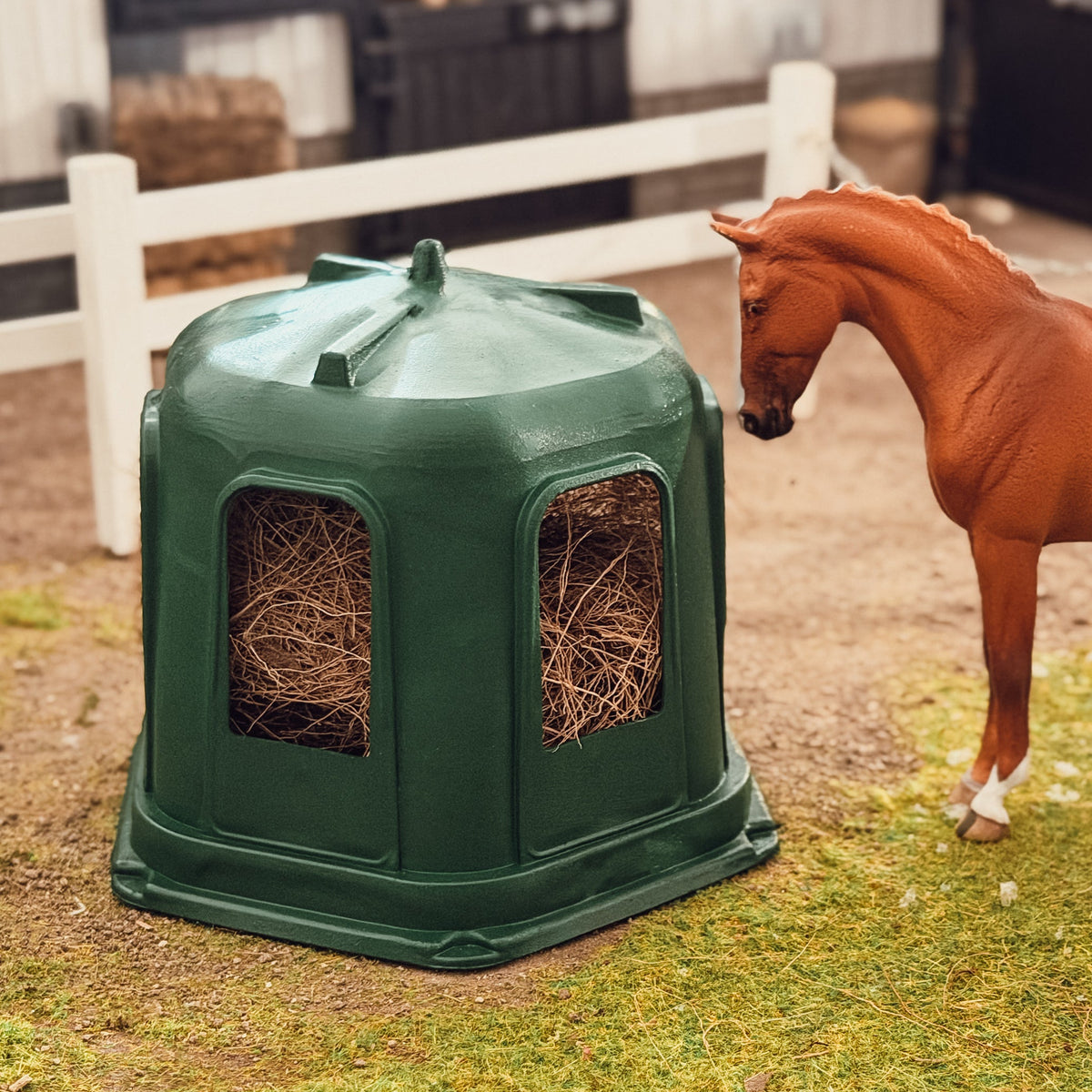 Schleich model horse looking at the green 3D printed hay bell feeder filled with hay