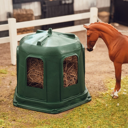 Schleich model horse looking at the green 3D printed hay bell feeder filled with hay