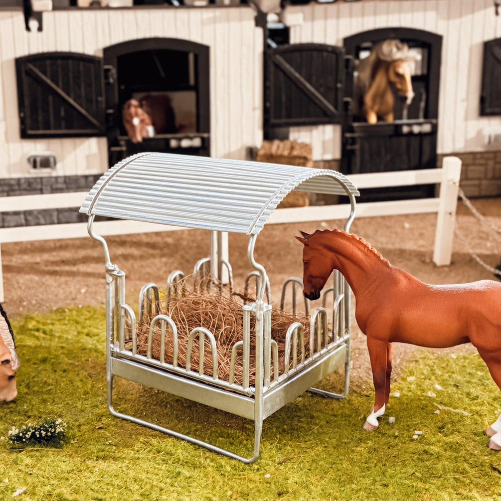 Covered hay rack for Schleich model horses set up in a stable aisle, with a chestnut horse feeding beside it and two horses in their stalls