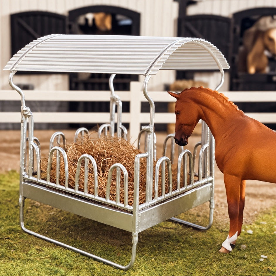 Silver 3D printed covered hay rack with curved canopy roof, filled with hay, next to a chestnut Schleich model horse in a stable yard
