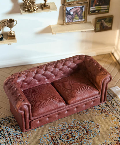 Top view of a miniature tufted couch with two cushions in a model horse clubhouse, with trophies and framed horse pictures on the wall