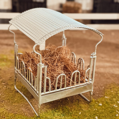 Close-up of the silver covered hay rack's curved corrugated canopy roof and U-shaped bars, filled with hay